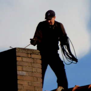 man sweeping chimney on roof
